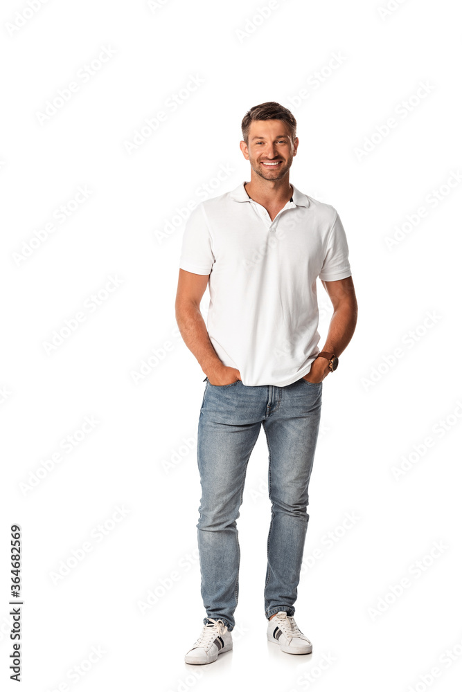 cheerful man in white t-shirt smiling while standing with hands in pockets on white