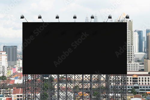Blank black road billboard with Kuala Lumpur cityscape background at day time. Street advertising poster, mock up, 3D rendering. Front view. Concept of marketing to promote or sell services or ideas.