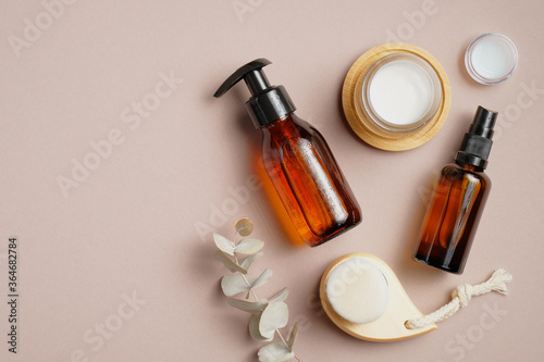 Bathroom cosmetics and accessories on brown background. Flat lay, top view. Pump bottle, cosmetic spray lotion, candles, body clean brush, eucalyptus leaf. photo