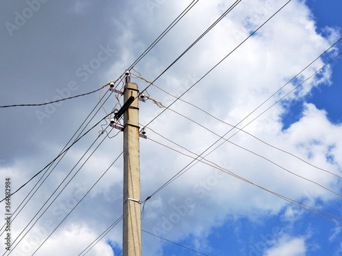Electric pole and intersecting wires on a background of blue sky and clouds. Illustration on the theme of electricity transportation, electrification of the countryside, rising energy prices