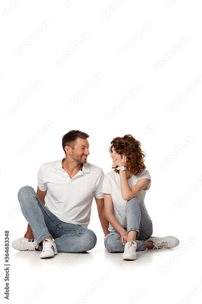 happy couple in denim jeans sitting and looking at each other on white happy couple in denim jeans sitting and looking at each other on white