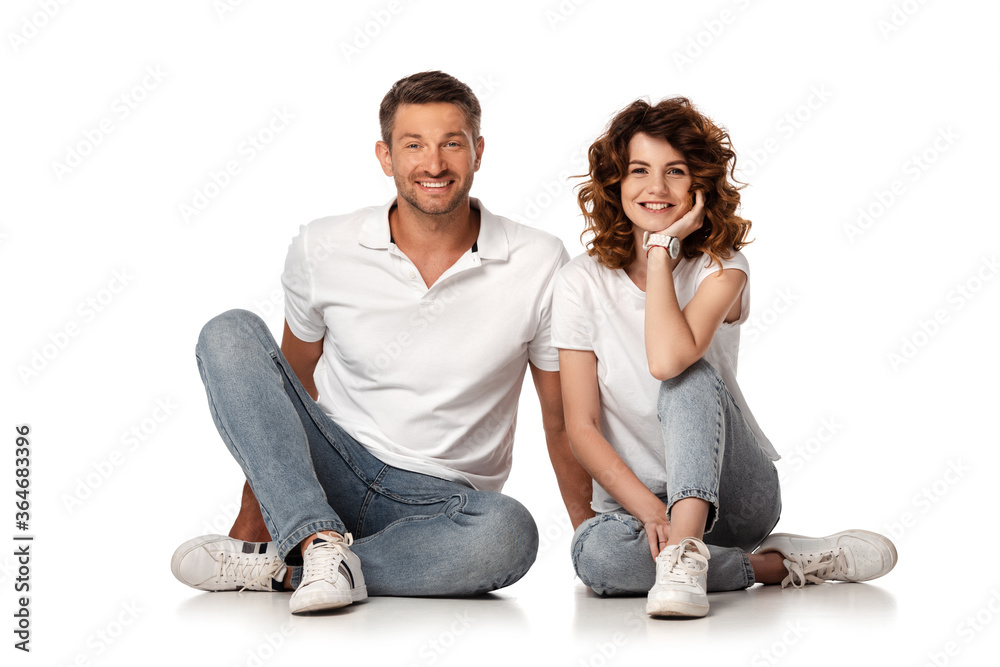 happy couple in denim jeans sitting and looking at camera on white happy couple in denim jeans sitting and looking at camera on white