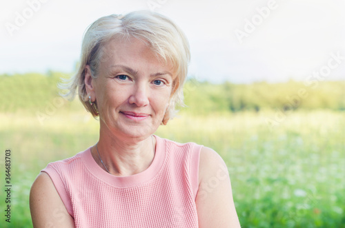 Portrait of positive senior adult elegant mature middle aged blonde woman outdoors in summer background with copy space. Attractive lady, female posing