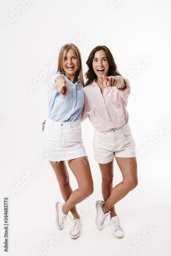 Image of smiling two women pointing fingers at camera while hugging
