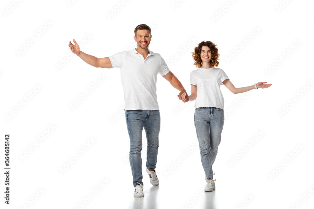 happy woman and cheerful man holding hands while walking on white