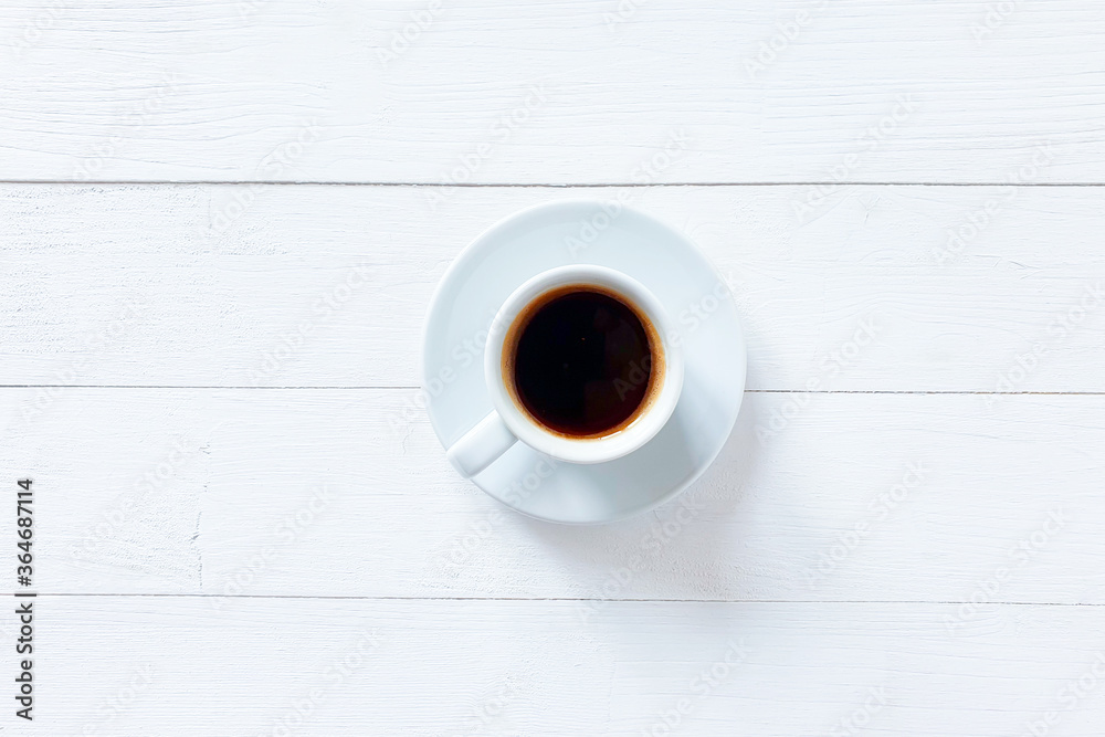 White cup with black coffee on a white wooden table. Top view, lifestyle. White cup with black coffee on a white wooden table. Top view, lifestyle.