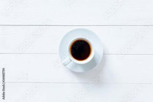 White cup with black coffee on a white wooden table. Top view, lifestyle.