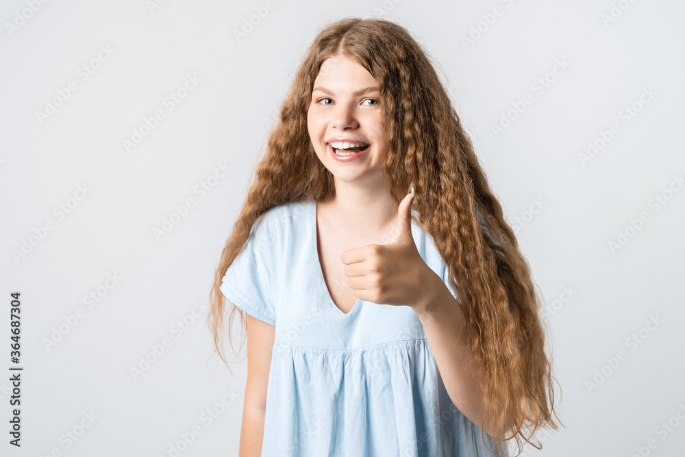 Good job. Pretty carefree modern stylish European girl with curly long hair making gesture OK, as if saying that everything is finee, white background.