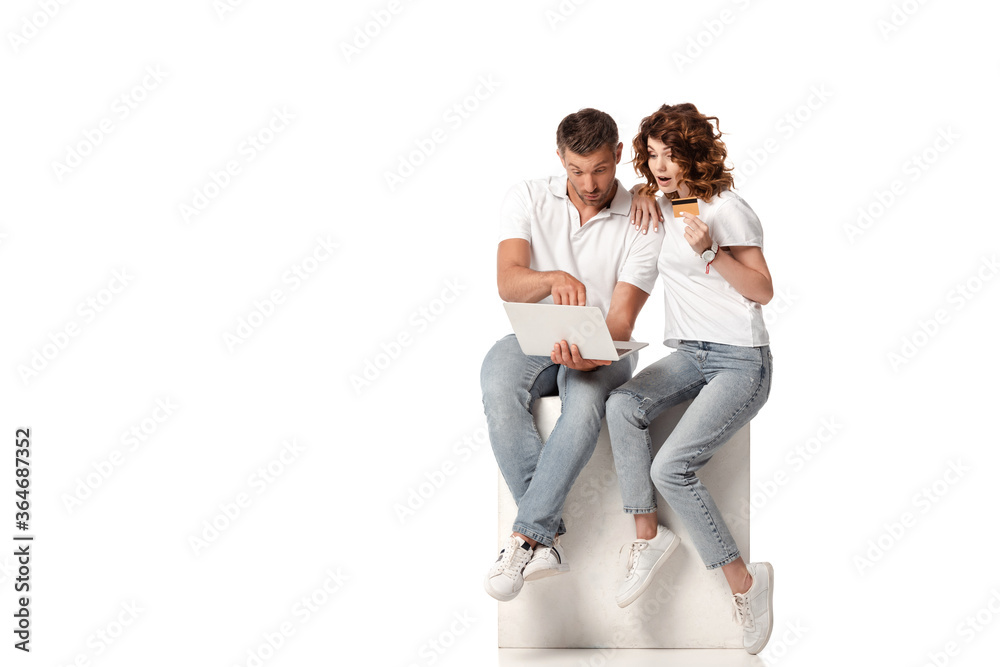 surprised woman holding credit card near man using laptop on white surprised woman holding credit card near man using laptop on white
