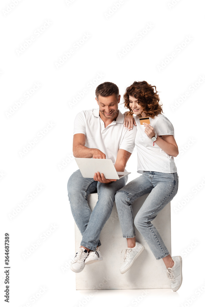 happy woman holding credit card near man using laptop on white happy woman holding credit card near man using laptop on white