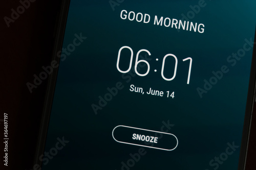 On a black smartphone, an alarm clock rings for 6 am with the inscription Good morning close-up, background photo