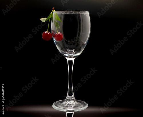 Pair of ripe cherries in an empty wine glass on a black background. Natural product. Natural color. Close-up.