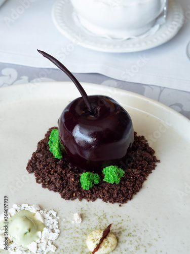 Chocolates in the shape of a chocolate apple. Sprinkled with chocolate chips, meringues and ice cream. Served on a white plate. Dert in a restaurant. A good treat. photo