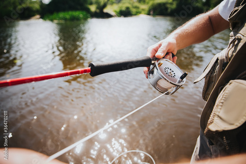 Young fisherman fishing on lake or river. Cut view of rod in guy's hand. Professional river hobby. Catching fish using rod. Cut view. Sunny day.