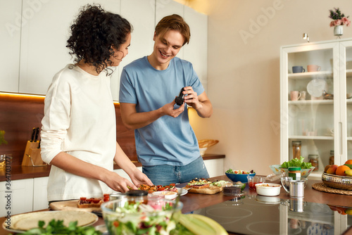 This is how we do it. Cheerful couple recording video blog about vegetarian healthy food on camera in the kitchen. Young man and woman cooking breakfast. Vegetarianism, diet, stay home concept