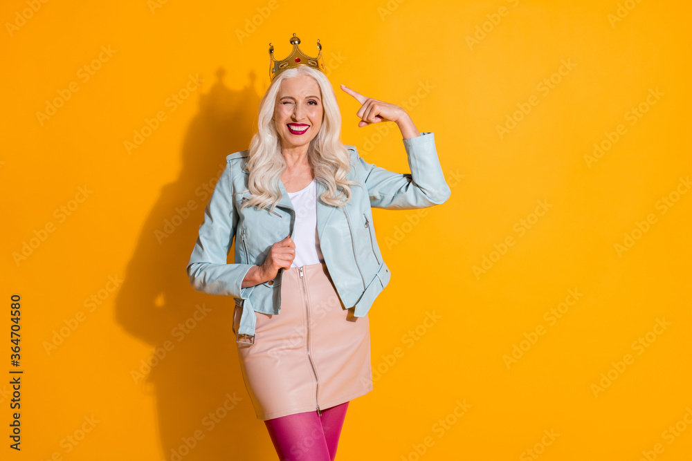 Portrait of positive cheerful old woman demonstrate her party win point index finger golden crown wink blink wear good look pink stockings isolated over bright shine color background