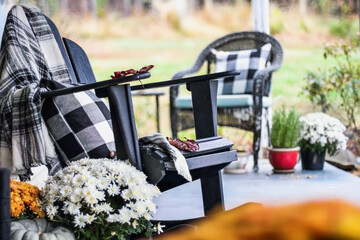 Adirondack rocking chair with style buffalo check blanket and pillows on a porch or patio decorated for autumn with heirloom gourds & white and orange mums. Selective focus with garden in background.