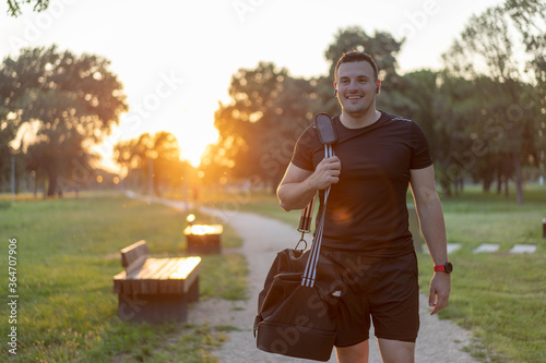  Attractive Man walking in a park after workout, wearing sport bag and smiling.