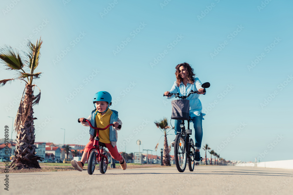Fototapeta premium Little kid riding a balance bike with his mother on a bicycle