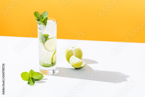 Fresh Mojito cocktail with lime and mint in highball glass with water drops on white and yellow background in bright sun light, Mojito refreshing drinks. Copy space, summer vacation and party concept