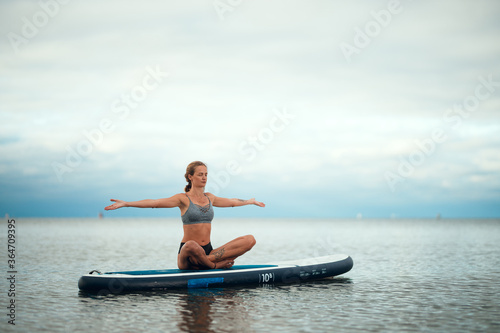 Woman practicing yoga on the paddle board in the morning