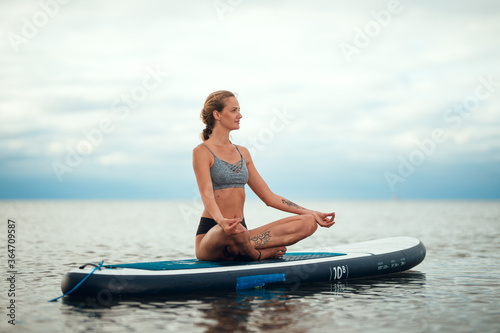 Woman practicing yoga on the paddle board in the morning