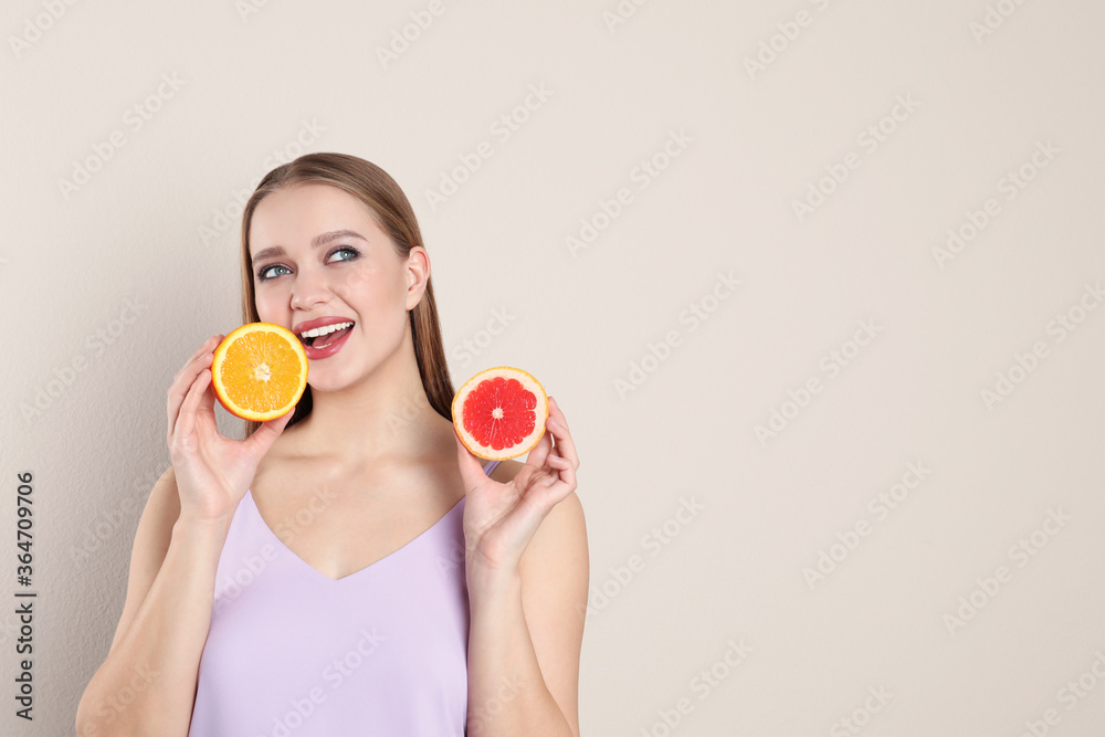 Young woman with cut orange and grapefruit on beige background, space for text. Vitamin rich food Young woman with cut orange and grapefruit on beige background, space for text. Vitamin rich food