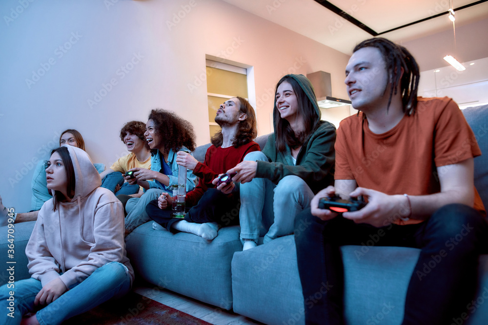 Teenagers relaxing at home. Group of young multicultural people playing video games and smoking marijuana from a bong while sitting on the couch