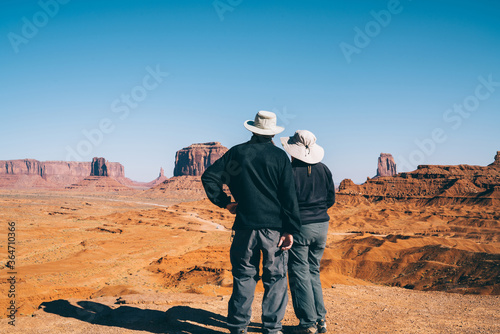 Back view of male and female american tourists observing beautiful landscape of Monument valley,couple of travelers enjoying excursion to famous american landmark together looking at stone formation.