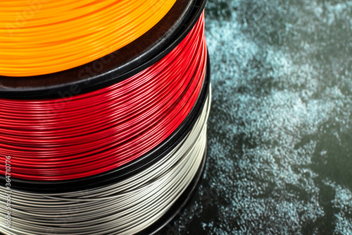 Three coils of filament for 3d printing. Bright thermoplastic of orange, red and grey colors.