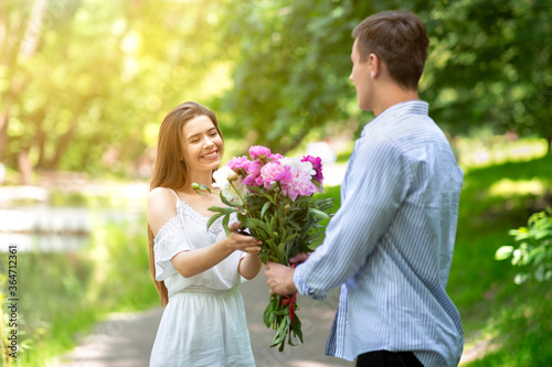 Celebrating anniversary. Loving young husband surprising his wife with flower bouquet outdoors