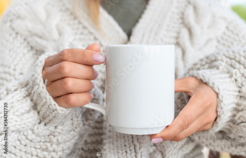 White ceramic mug mockup. Woman in Sweater Holding a Warm Cup of Coffee. Copy space for your print