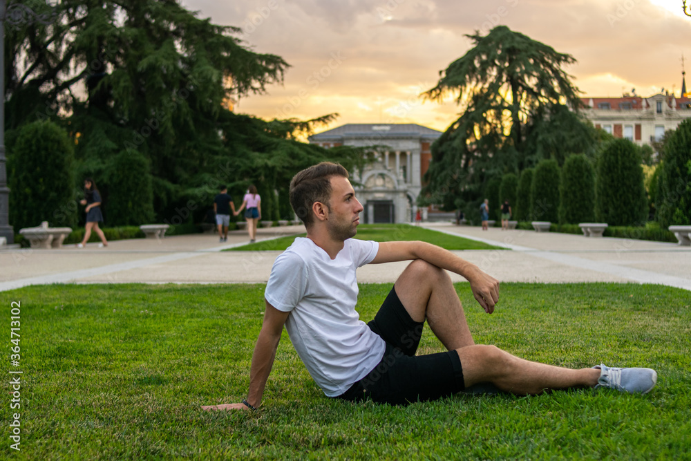 Fototapeta premium Photo of a young and attractive man sitting relaxed on the grass looking to the horizon