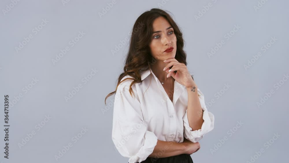 Brunette model in white shirt and black skirt has folded her hands and looking at something being unpleased. Posing on gray background. Close up Brunette model in white shirt and black skirt has folded her hands and looking at something being unpleased. Posing on gray background. Close up
