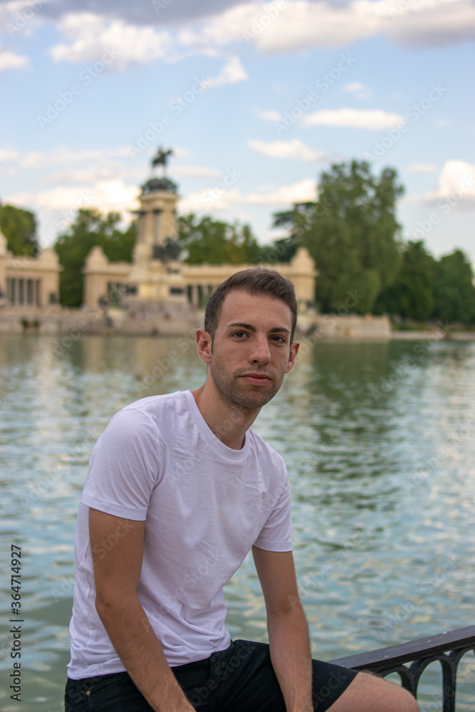 Photo of a young and attractive man with a white t/shirt standing next to the lagoon in Retiro park, Madrid