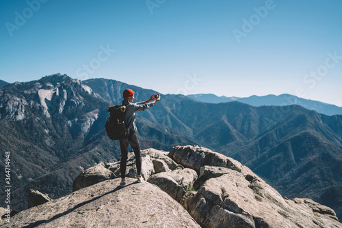 Active female traveler with touristick backpack using smartphone for making selfie on breathtaking nature view,girl blogger taking photo on cellphone during adventure journey in national park