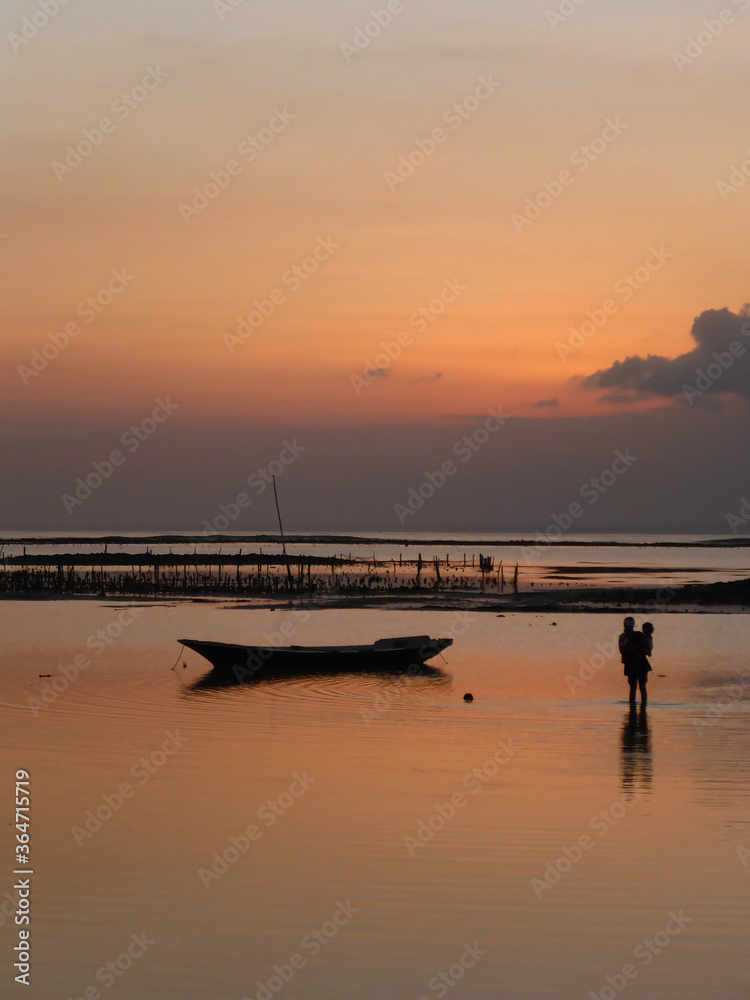 Woman holding a child wading in shallow waters of Lembongan, Bali at dusk