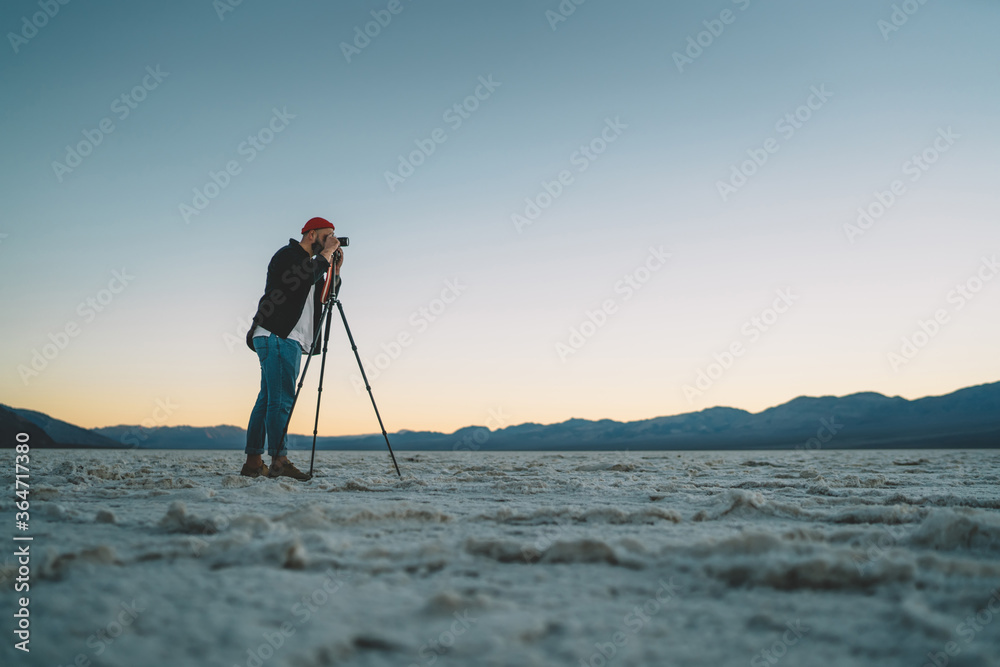 Young professional photographer shooting video of sunset in Badwater basin during trip, skilled male journalist taking picture of expedition to death valley photographing beautiful landscape .