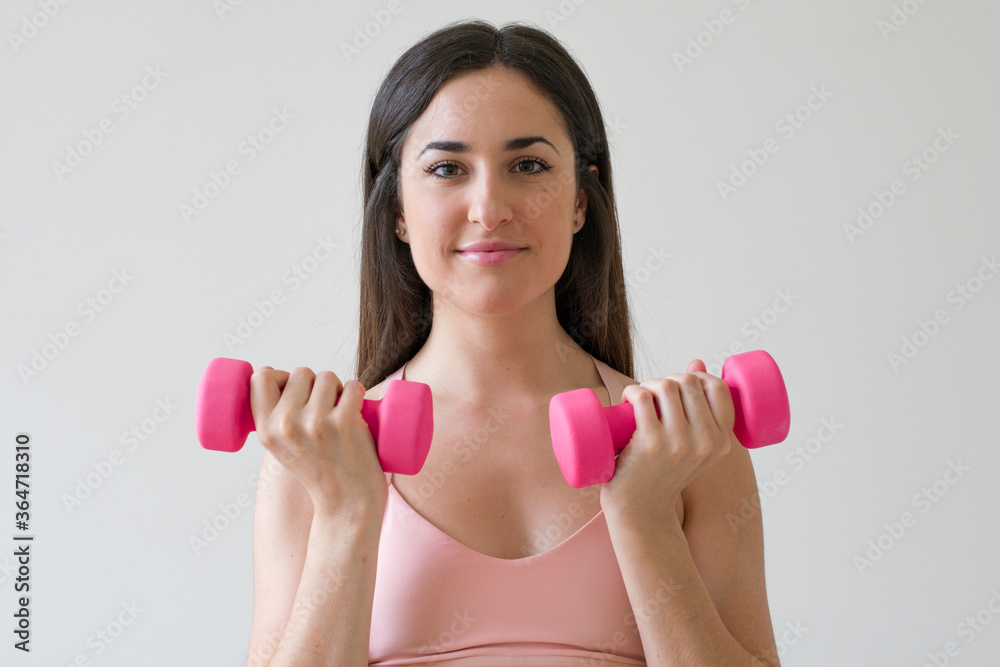 Young brunette woman exercising with pink dumbbells in front of a white background Young brunette woman exercising with pink dumbbells in front of a white background