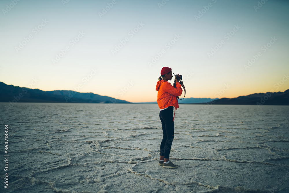 Skilled female photographer taking photo of wild environment and landscape during expedition, hipster girl using professional equipment for taking pictures at twilight in death valley in america.