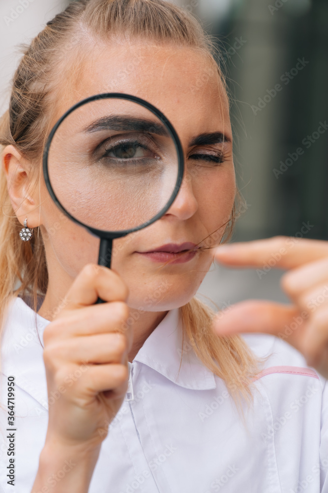 portrait of doctor woman who holds a magnifying glass and shows a small size portrait of doctor woman who holds a magnifying glass and shows a small size