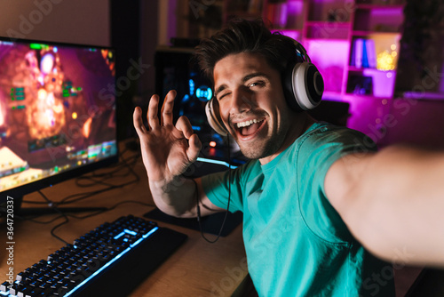 Photos Image of man gesturing ok sign and taking selfie while playing game