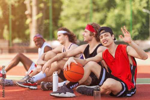 Group of basketball players resting at outdoor court after match, free space