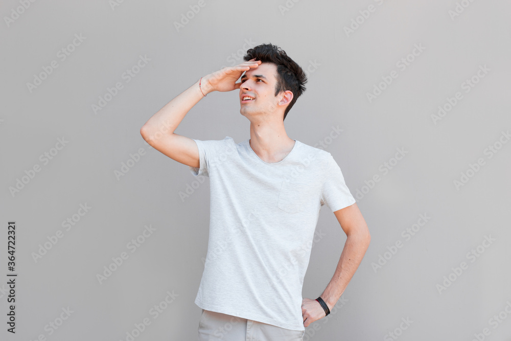 Charming handsome. Handsome young man in casual wear keeping arm near face and smiling while standing isolated on grey background Charming handsome. Handsome young man in casual wear keeping arm near face and smiling while standing isolated on grey background