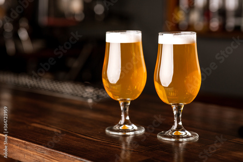Date at pub. Glasses with light beer and foam on wooden bar counter in interior of pub