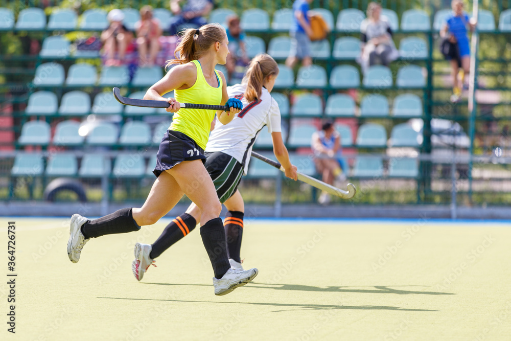 Young women playing field hockey game on the pitch