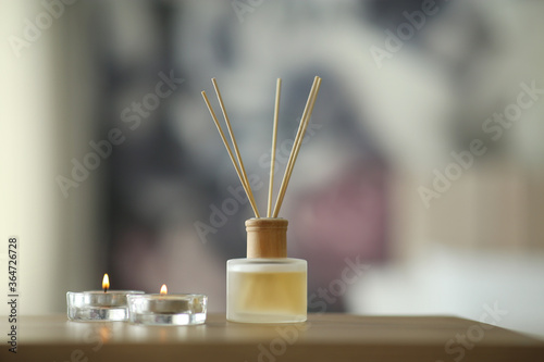 Aromatic reed air freshener and scented candles on table indoors