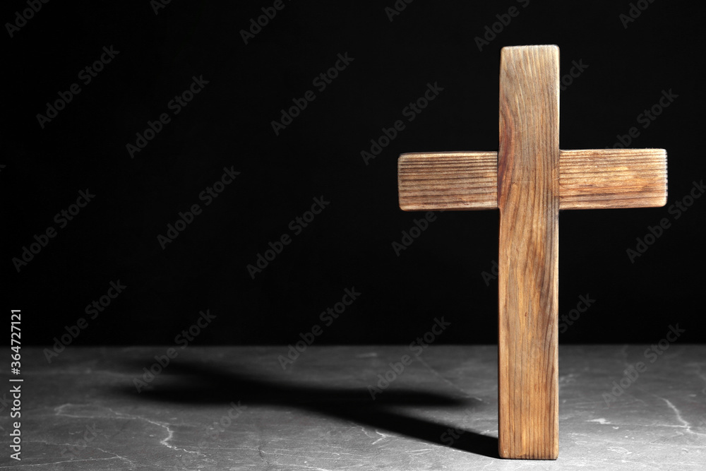 Wooden Christian cross on brown marble table against black background, space for text. Religion concept