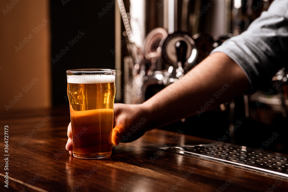 Craft beer for regular client. Bartender gives glass of light lager in interior of pub