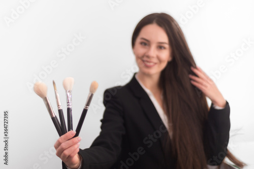 girl, makeup artist, with long dark hair in a business suit holding a brush on an outstretched hand, on a white background